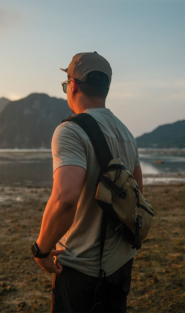 Ryan walking down a beach on sunset while wearing a backpack and a cap