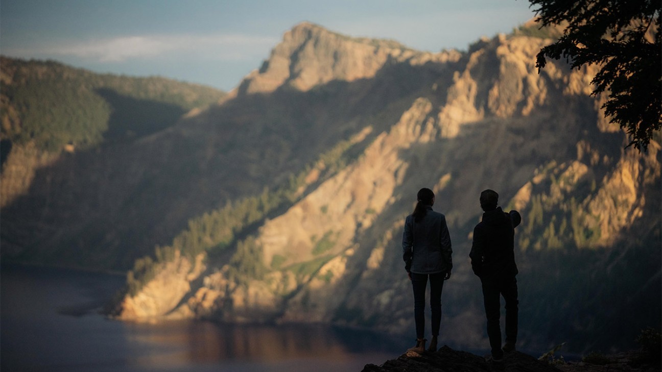 A man and a woman stand on a viewpoint overlooking a mountain range in Oregon.