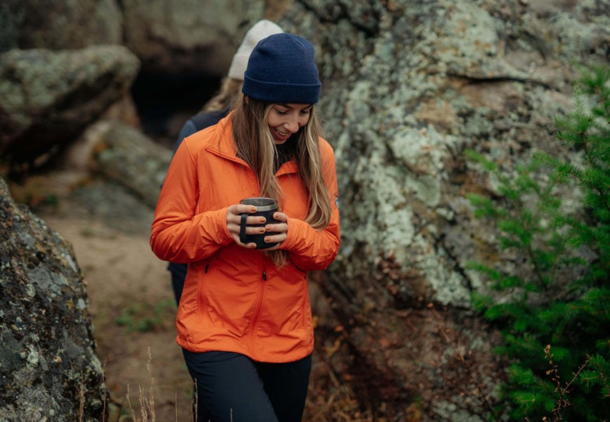 A woman in The One Jacket strolling on a trail with a mug