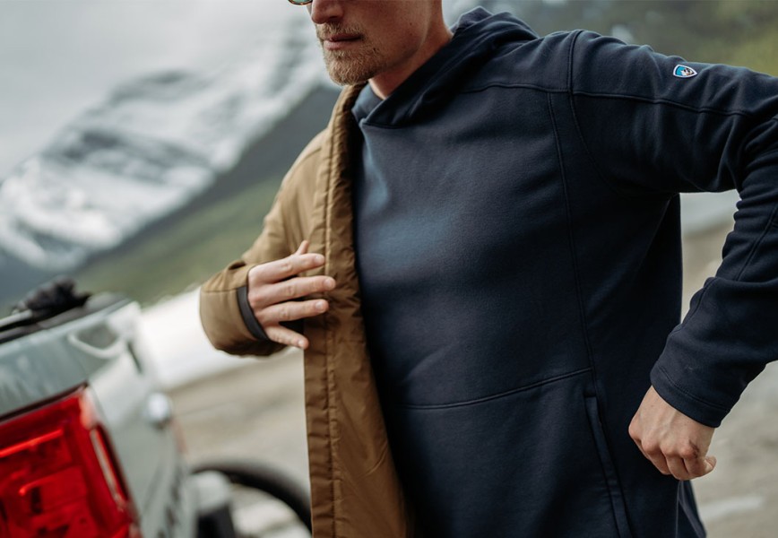 A man dressing up in fall jacket with mountainside in the background