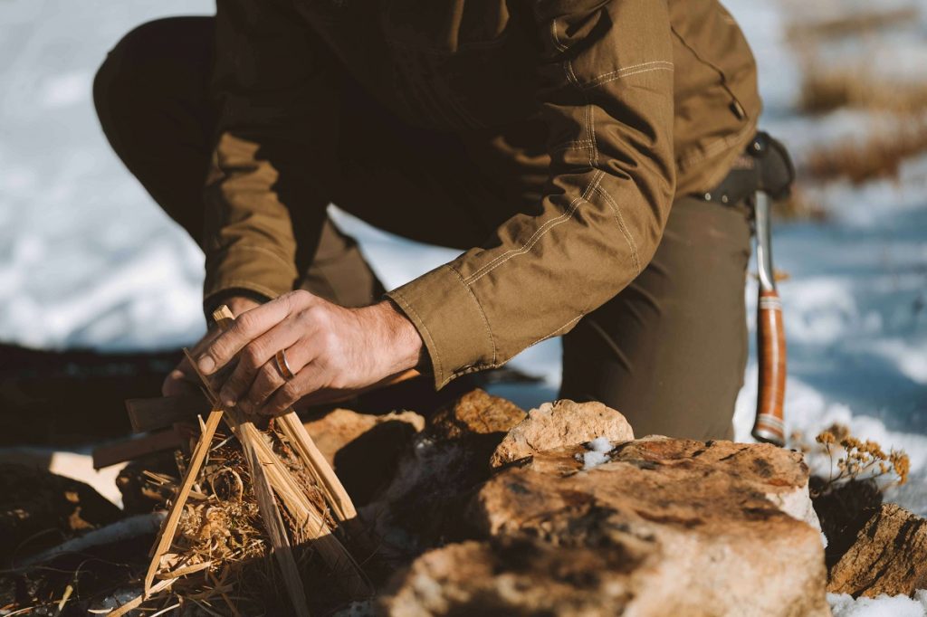 man in brown jacket holding wood on snowy ground