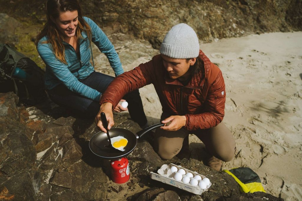 man in red jacket holding frying pan with eggs in the outdoors