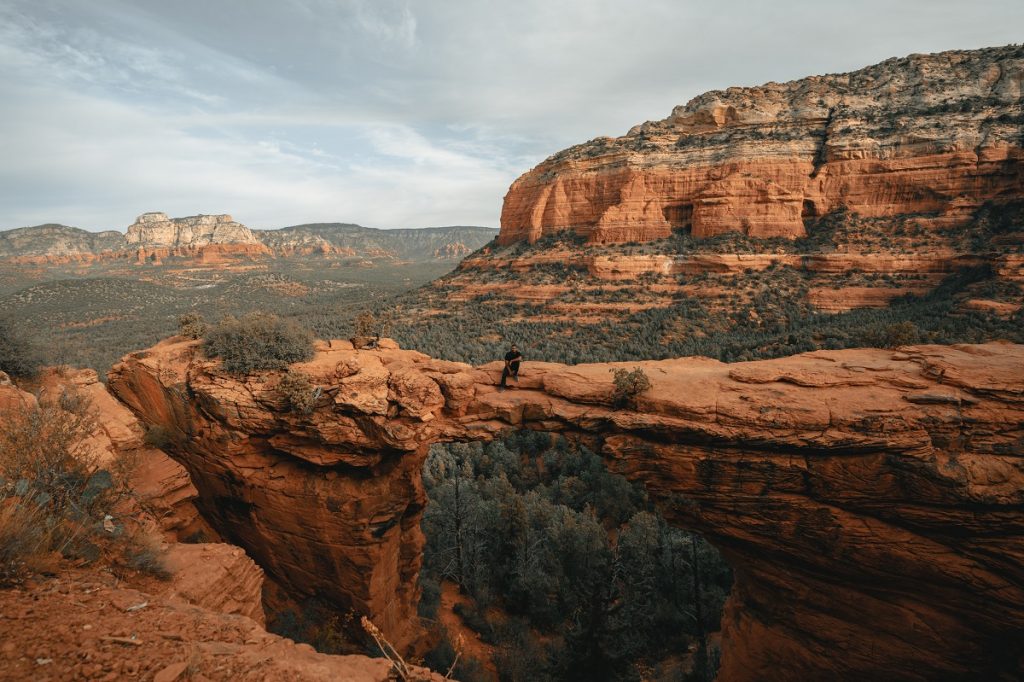 man sitting on top of brown rock mountain bridge during daytime