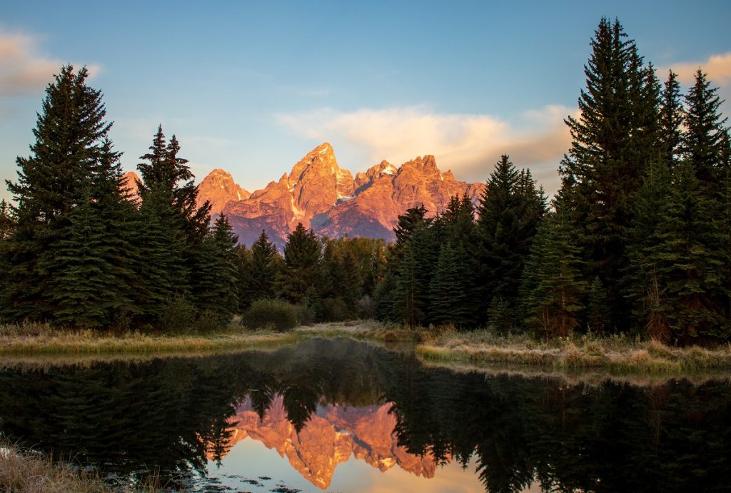 sunny mountains rising above the body of water surrounded by dark trees