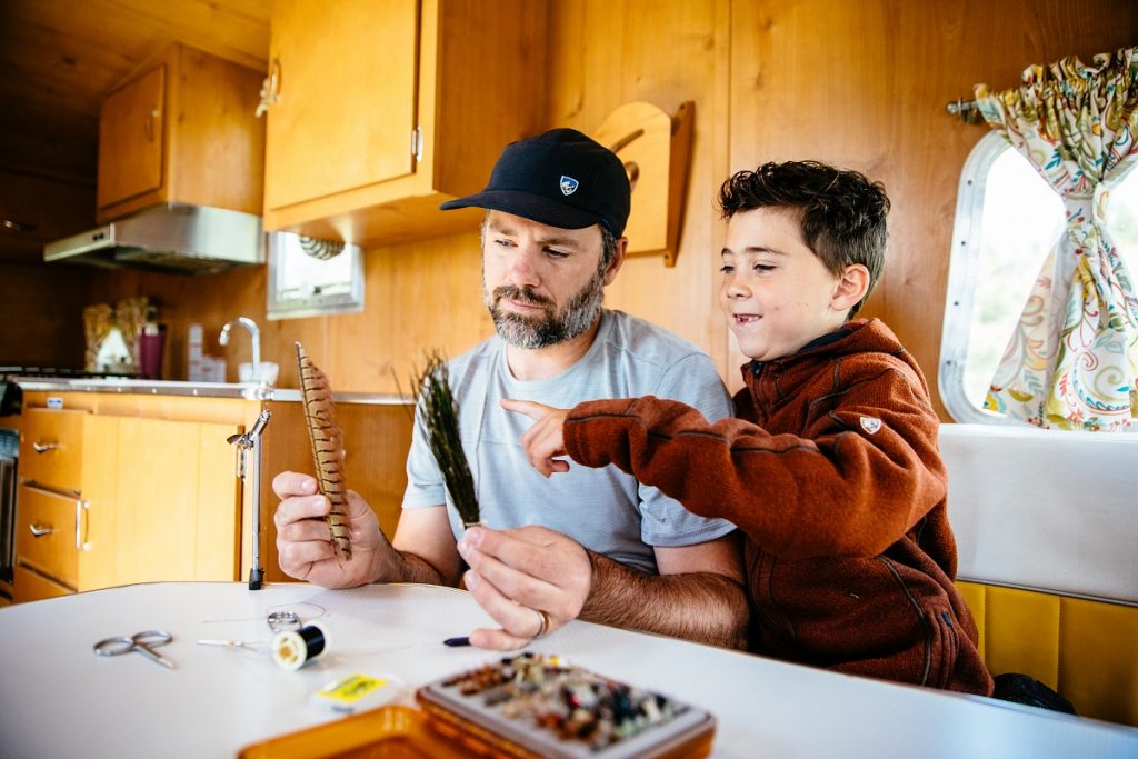 man in KÜHL shirt showing feathers to his son in camper