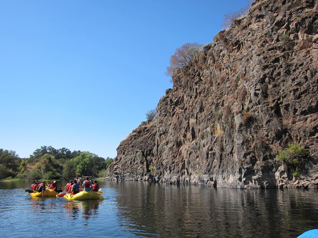 yellow boat rafting next to rocky cliff