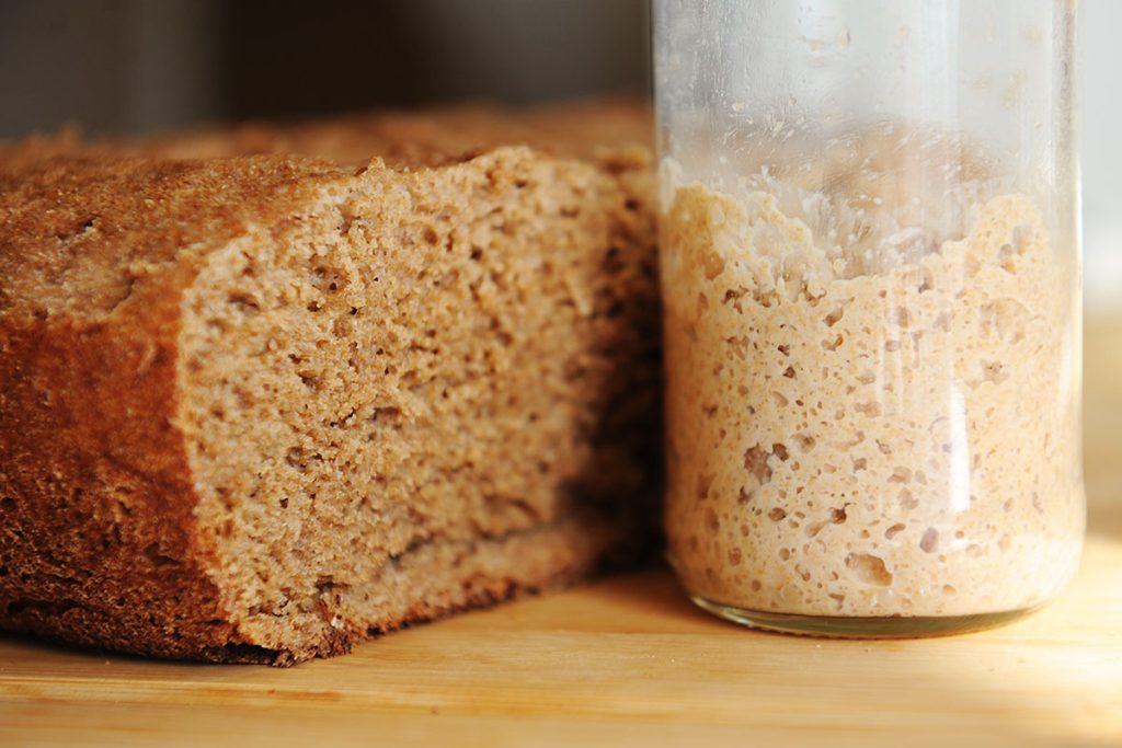 Sliced freshly baked homemade rye-wheat whole grain bread and rye sourdough in a glass jar. Close up